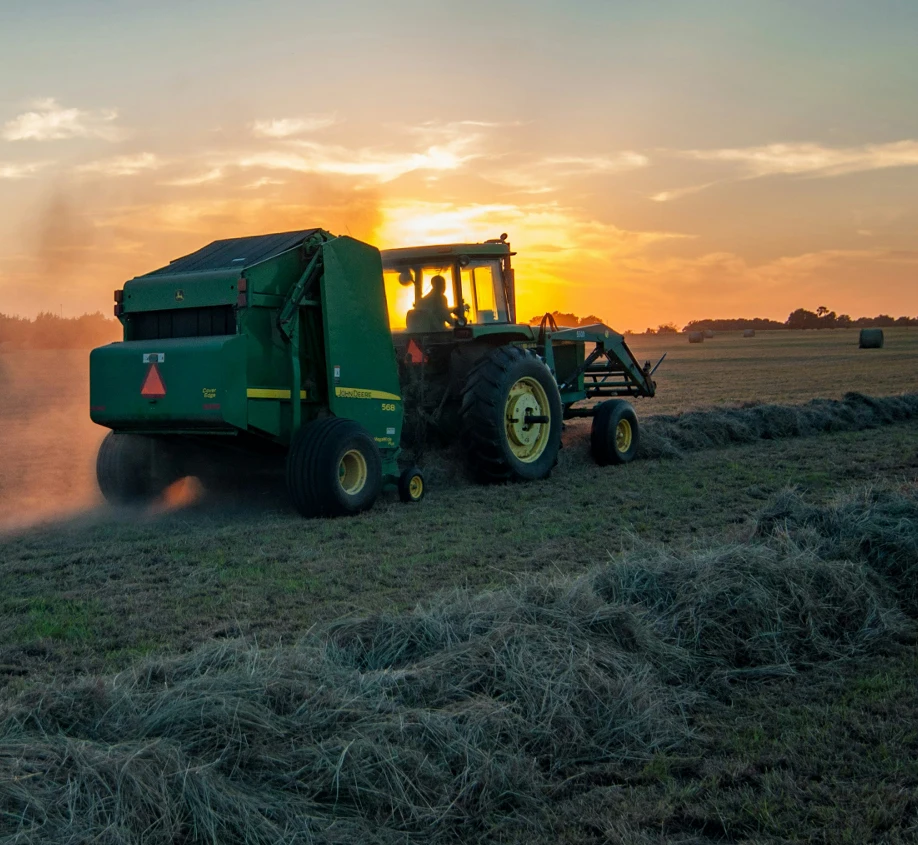 traktor balíkuje seno při západu slunce